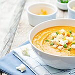 Creamy soup topped with cauliflower, croutons, and green onions in a white bowl on a folded blue napkin.