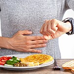 Person checking a smartwatch while seated at a table with a low-carb meal, bread slices, and breakfast utensils.