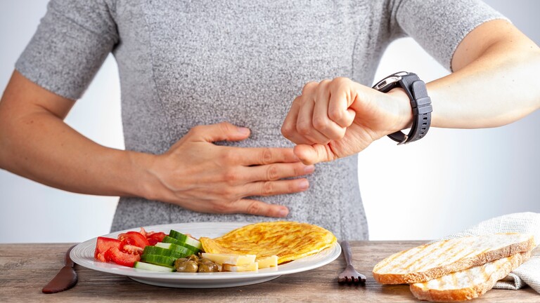 Person checking a smartwatch while seated at a table with a low-carb meal, bread slices, and breakfast utensils.