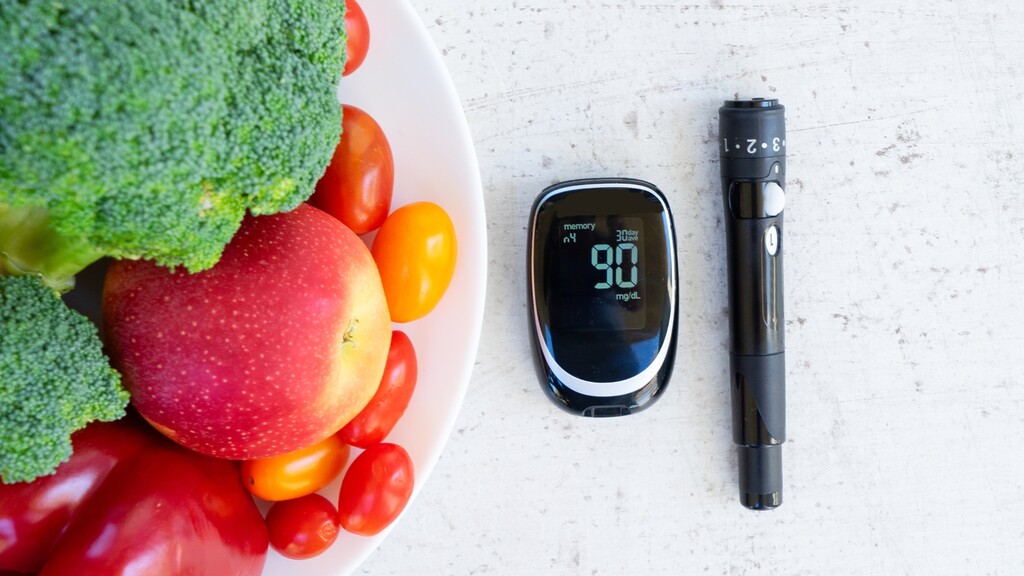 Blood glucose meter beside fresh vegetables and fruit.