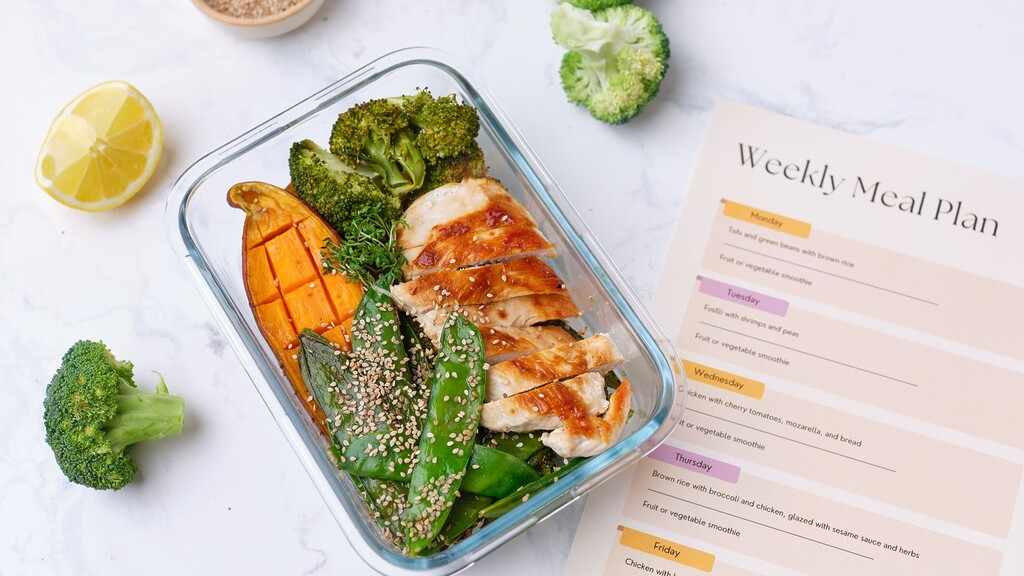 Chicken and vegetables in a meal prep container beside a weekly meal plan.