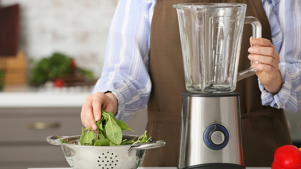 Person preparing leafy greens beside a blender.