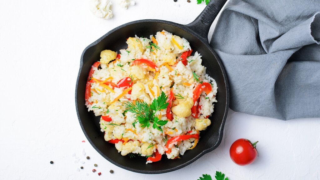 Cauliflower rice with vegetables and herbs served in a black cast iron skillet on a white surface.