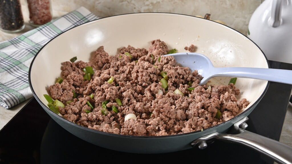 Ground meat cooking in a skillet with green onions.