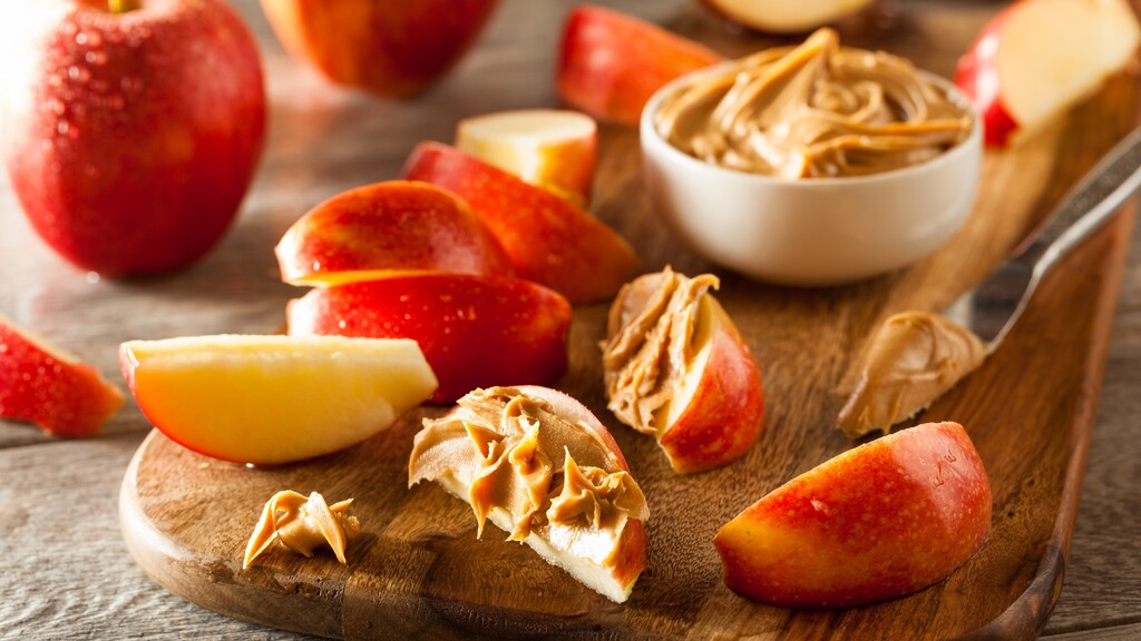Apple slices served with peanut butter on a wooden cutting board, showing a fiber-rich fruit snack paired with healthy fat.