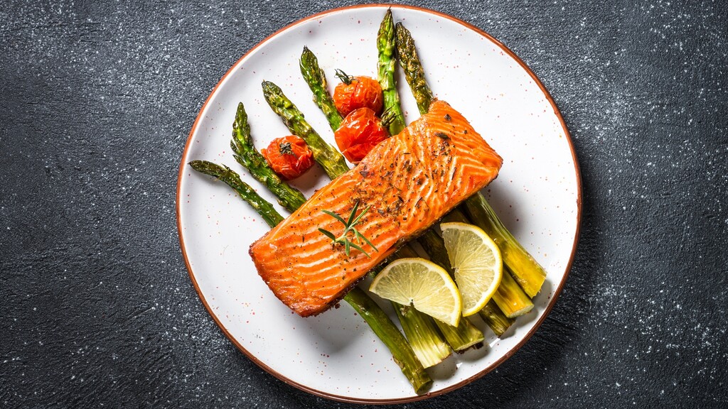 Grilled salmon served with asparagus, roasted tomatoes, and lemon slices on a white plate.