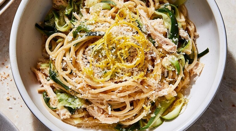 Lemon chicken spaghetti with zucchini ribbons, parmesan, and fresh lemon zest in a white bowl.
