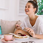 Woman smiling while eating a meal at a table.