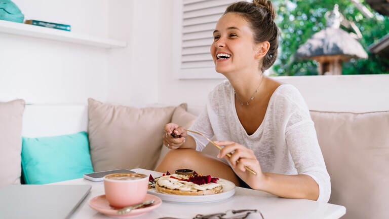 Woman smiling while eating a meal at a table.