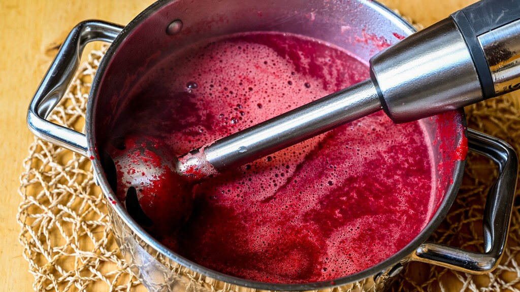 Immersion blender mixing bright red soup in a pot.