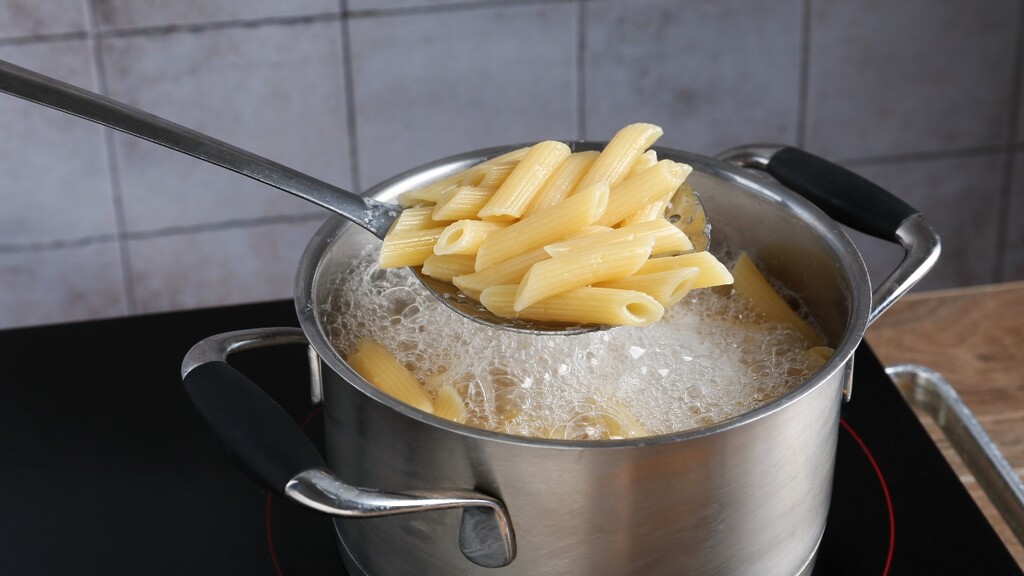 A wooden spoon stirring a pot of boiling water and penne pasta.