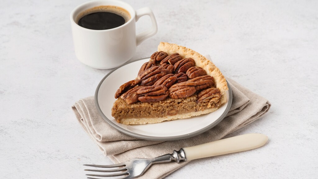 Slice of pecan pie served with black coffee.