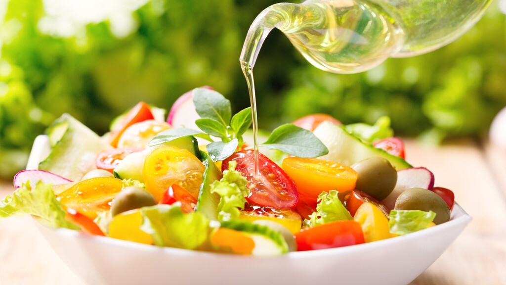 A steady pour of extra-virgin olive oil cascading over a bowl of vegetable pasta