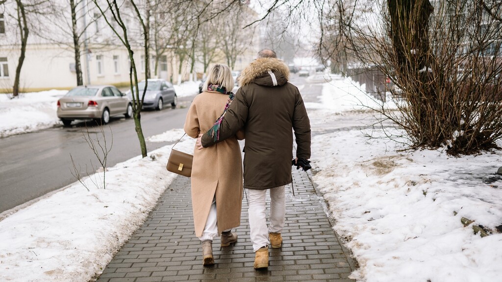 Couple walking together on a snowy sidewalk.