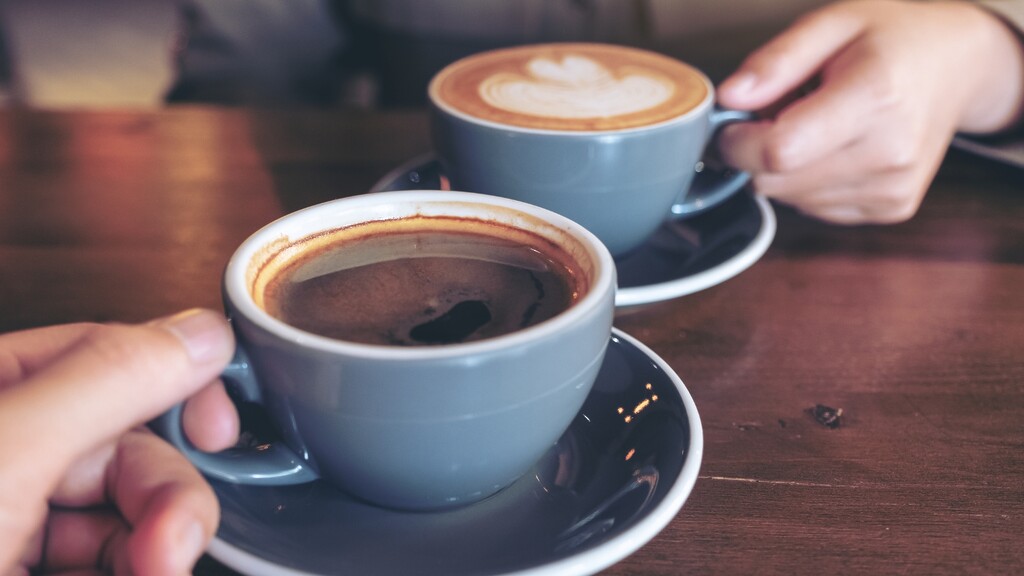 Two people holding cups of coffee at a table.