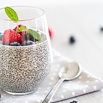 Chia seed pudding in a glass topped with raspberries, blueberries, and fresh mint on a bright white table.