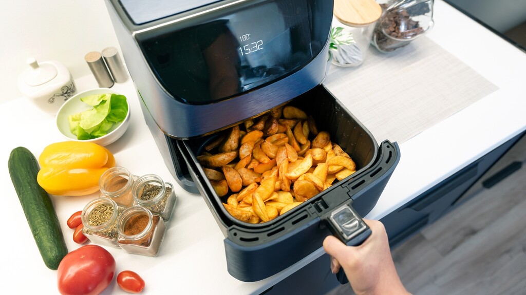 Air fryer basket filled with cooked potato wedges.
