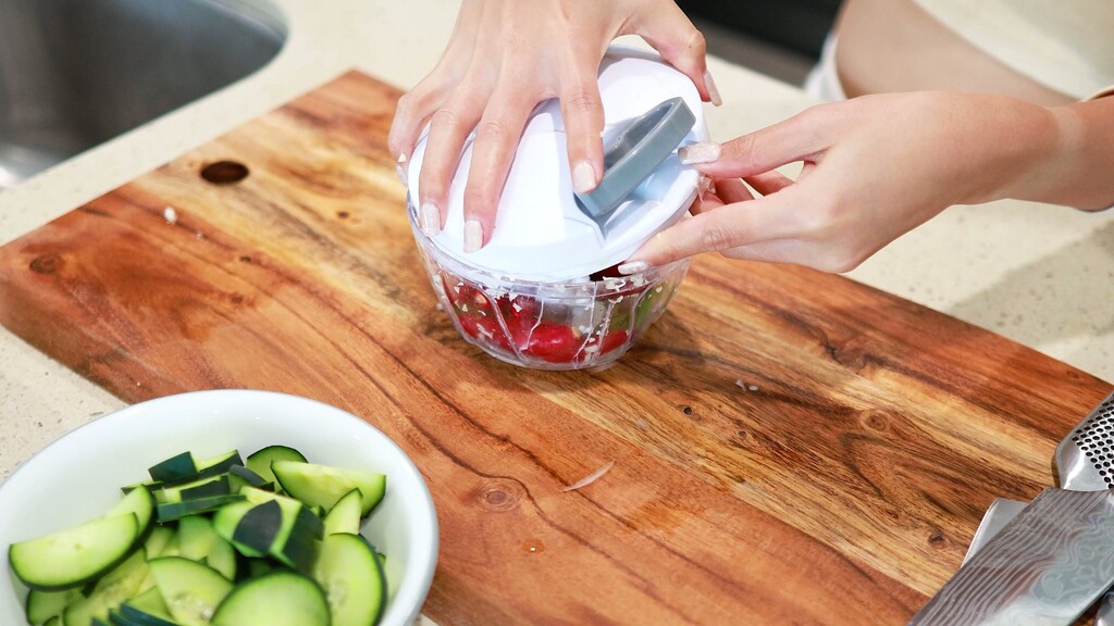 Hands using a food chopper on a cutting board.
