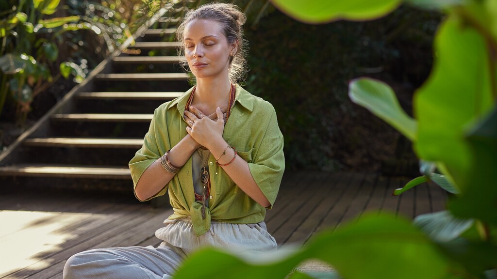 Woman meditating outdoors with hands over her chest.