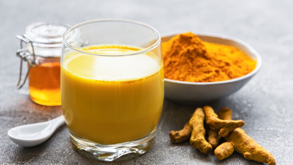 Golden turmeric drink with turmeric powder, fresh turmeric roots, and honey.