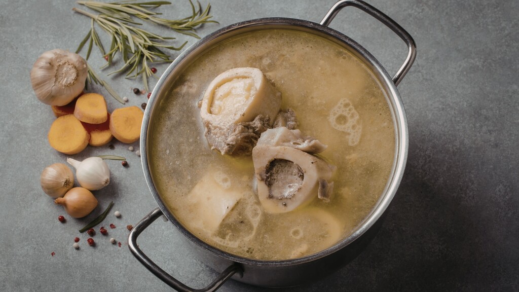 Pot of bone broth simmering with bones, garlic, onions, and herbs.