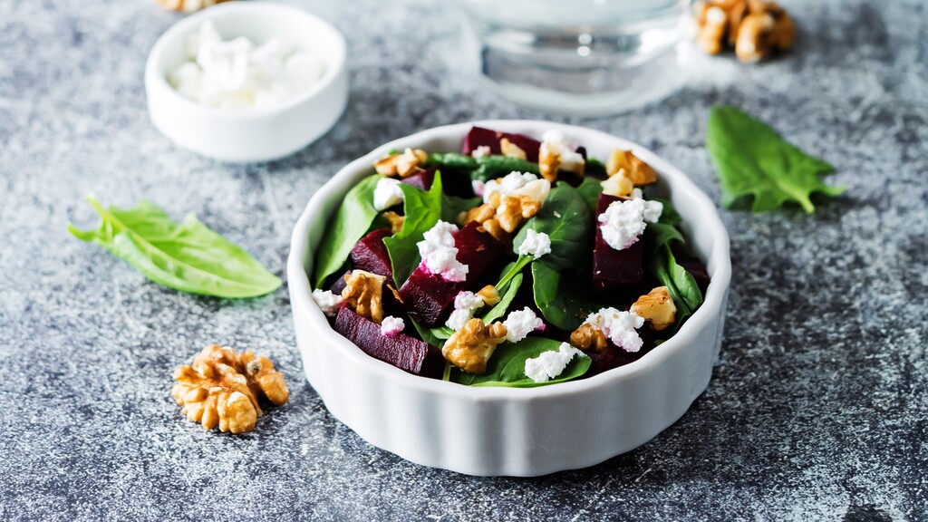 Spinach salad with walnuts, beetroot, and crumbled cheese in a white bowl.