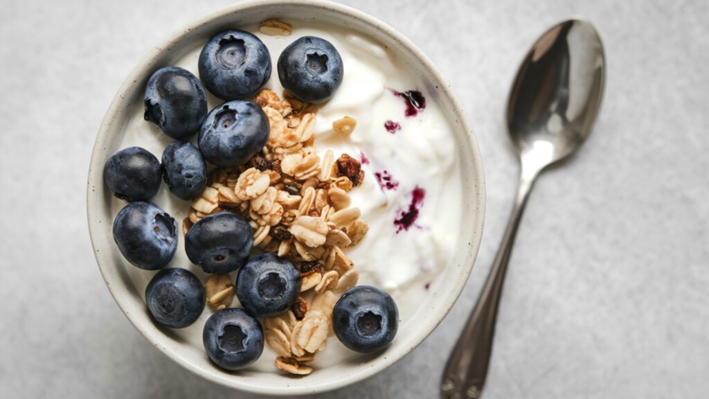 Yogurt bowl topped with blueberries and granola beside a spoon.