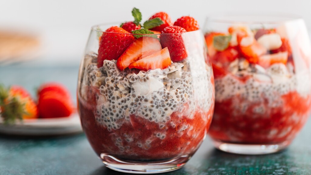 Chia seed pudding topped with strawberries and mint in glass cups.