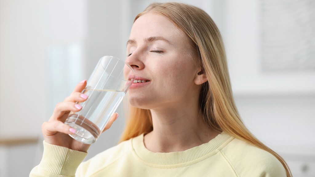 Woman calmly drinking a glass of water in a bright indoor setting.