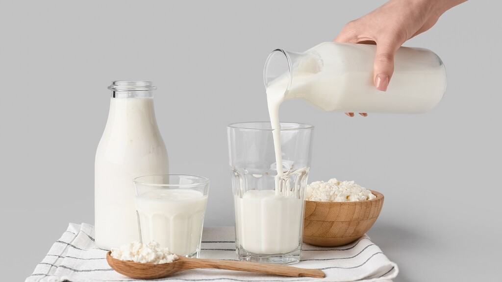 Kefir being poured into a glass beside a bottle of kefir and a bowl of curds.