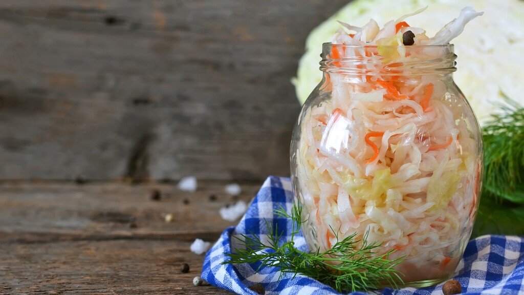 Jar of fresh sauerkraut with cabbage, dill, and spices on a rustic table.