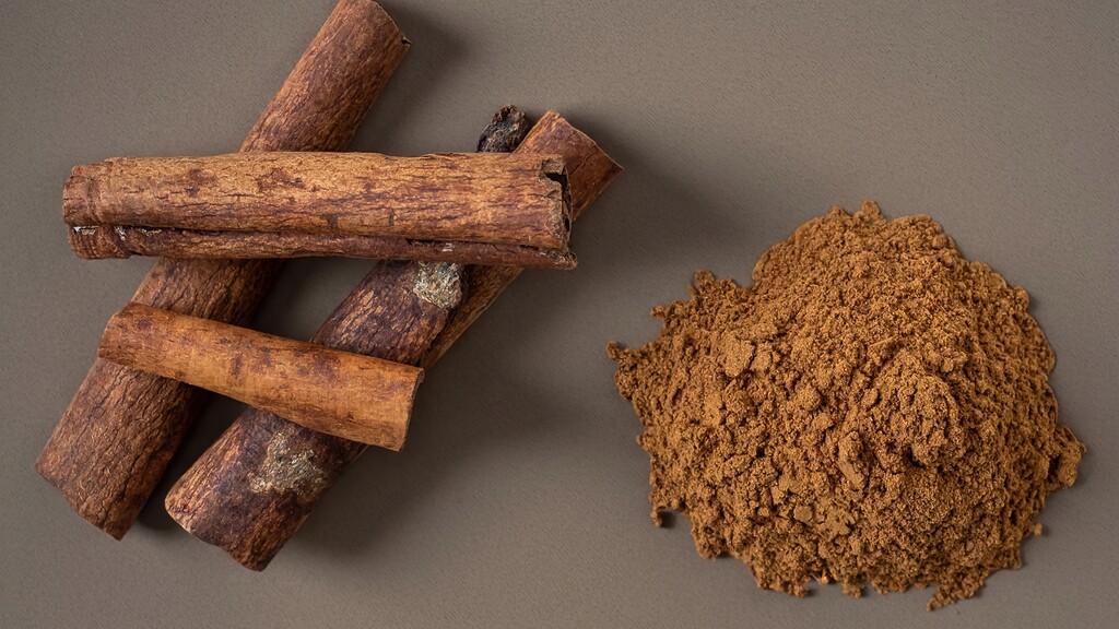 Cinnamon sticks tied with twine resting near a small spoonful of ground cinnamon