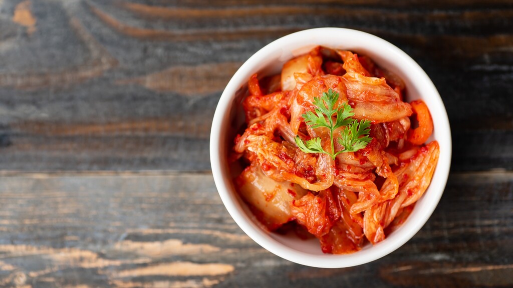 Bowl of spicy kimchi topped with fresh herbs on a dark wooden surface.