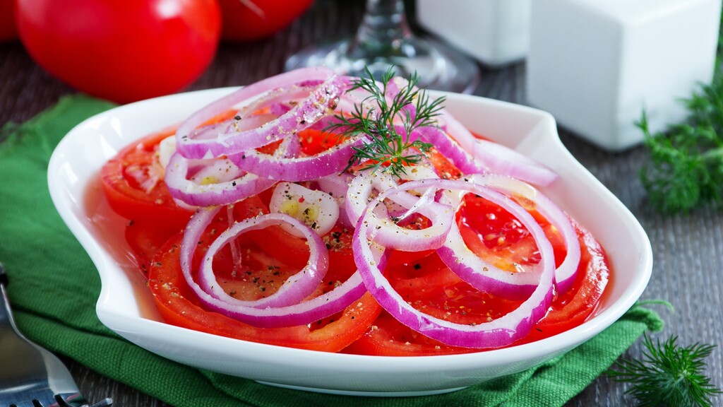 Sliced red onions and tomatoes served in a white dish with fresh dill.