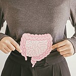 7 Morning Habits for a Calmer, More Predictable Gut Person pointing to a pink digestive system illustration over their abdomen, highlighting gut health and digestion.