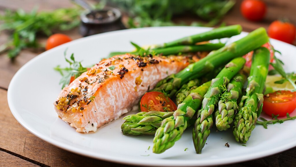 Plate of cooked salmon with asparagus spears and cherry tomatoes.