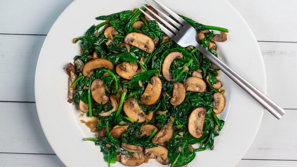 Sautéed spinach and sliced mushrooms on a white plate with a fork.