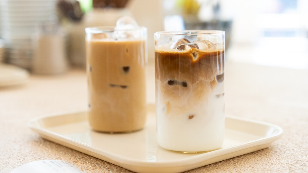 Two iced coffee drinks on a tray, one layered with oat milk and coffee.