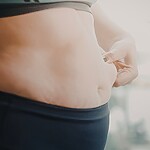 Close-up of a woman pinching belly fat, representing frustration with PCOS-related weight gain.
