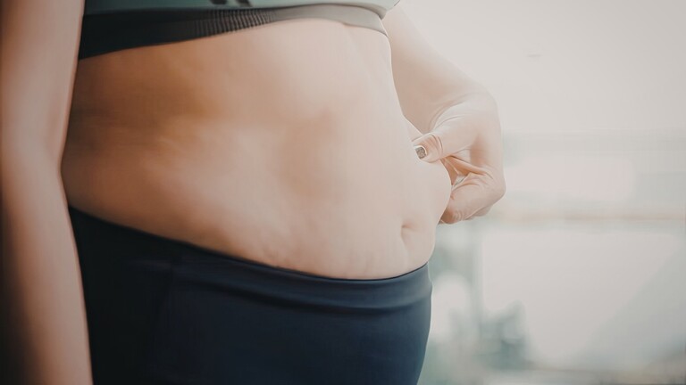 Close-up of a woman pinching belly fat, representing frustration with PCOS-related weight gain.