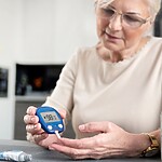6 Proven Ways to Maintain Stable Blood Sugar All Day Older woman checking her blood sugar with a glucose meter while sitting at a kitchen table.