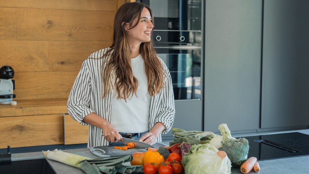 Woman preparing fresh vegetables on a kitchen counter with assorted low-carb produce in the foreground.
