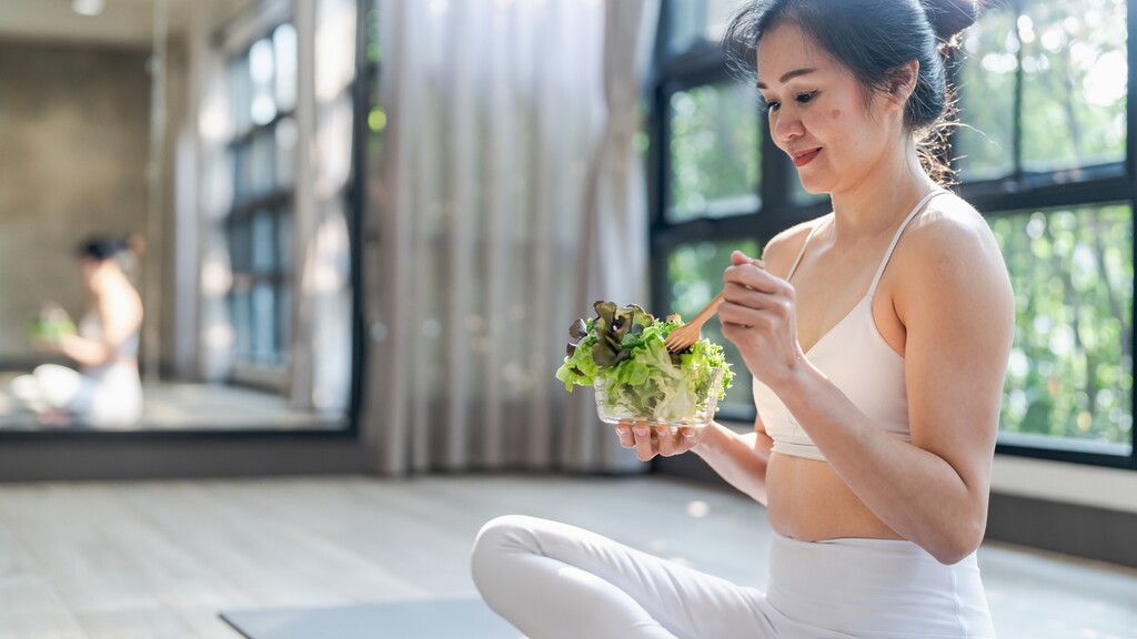 Woman eating a salad after exercise in a bright studio.