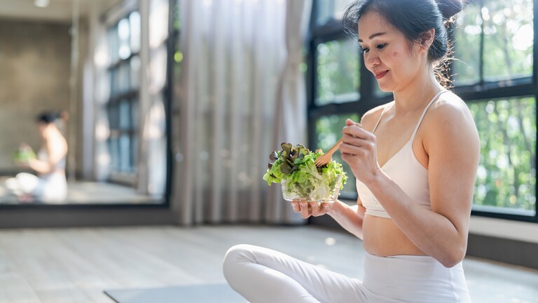 Woman eating a salad after exercise in a bright studio.