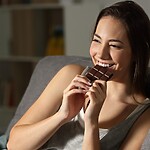 10 Unexpected Foods That Quietly Support Your Gut Health Woman eating dark chocolate on a couch.