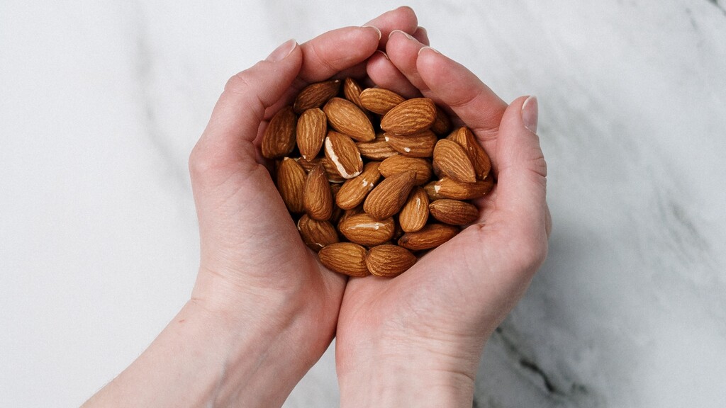 Almonds in hands: Pair of hands holding a handful of almonds over a light marble surface.