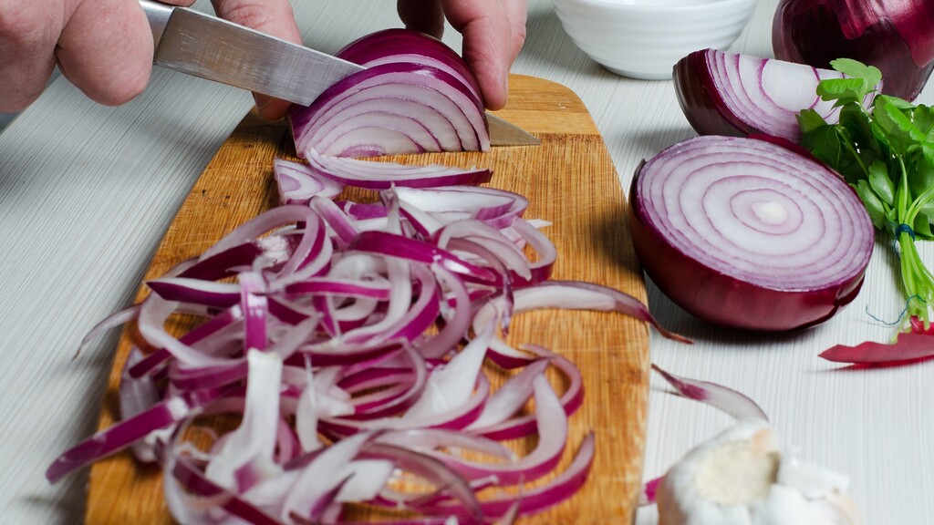 Red onion being sliced on a cutting board.
