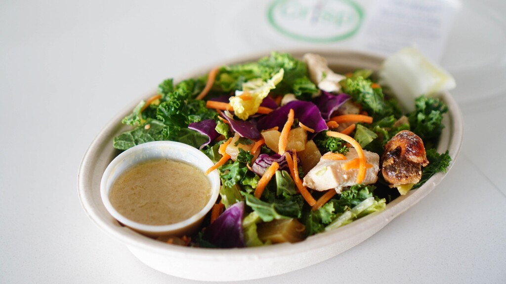 Salad bowl: Takeaway bowl of mixed salad with kale, carrots, purple cabbage, chicken, and dressing on the side.