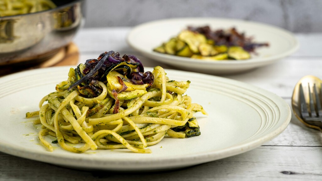 Pesto Zucchini pasta with vegetables served on a cream-colored plate.