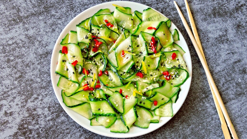 Cucumber ribbon salad with sesame seeds, red chili, and chopsticks.